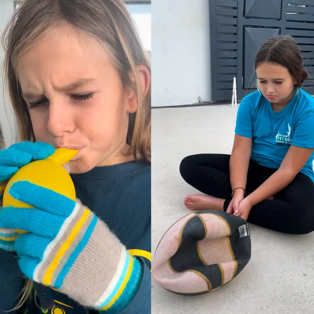 Child wearing gloves and a child sitting on the ground with a ball.